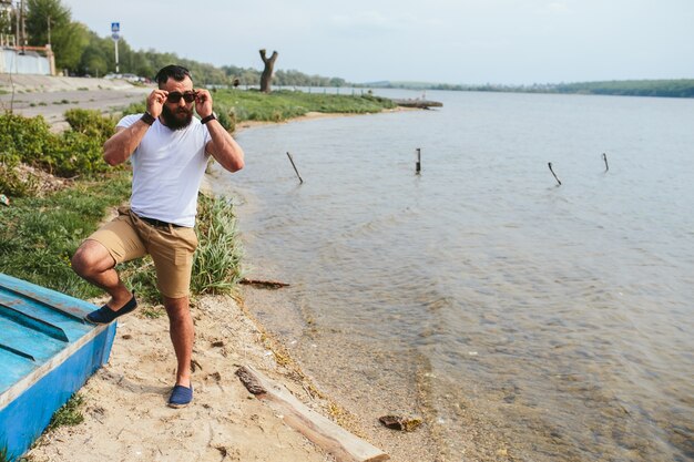 Stilvolle Mann mit Sonnenbrille am See aufwirft