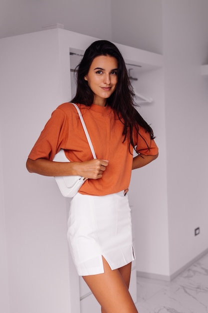 Stilvolle Mode junge kaukasische Frau Blogger zu Hause im Schlafzimmer tragen Ziegelfarbe Hemd und Rock