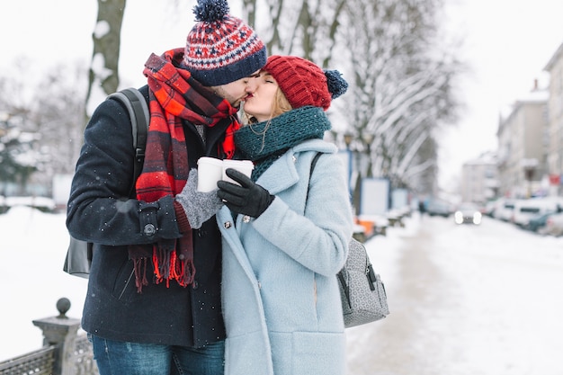 Stilvolle Paare auf schneebedeckter Straße küssen