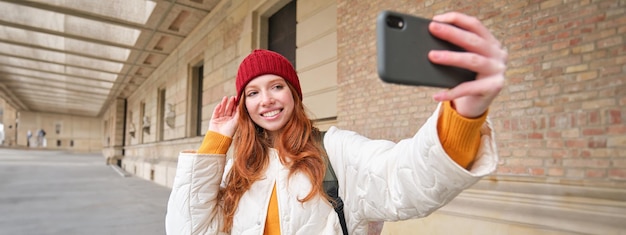 Kostenloses Foto stilvolle rothaarige touristin macht ein selfie vor einer touristenattraktion und macht ein foto mit dem smartphone