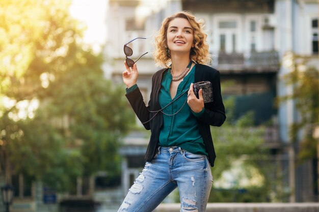 Stilvolle schöne Frau in Jeans und Jacke, die in der Straße mit kleinem Geldbeutel, elegantem Stil, Frühlingsmodetrends gehen