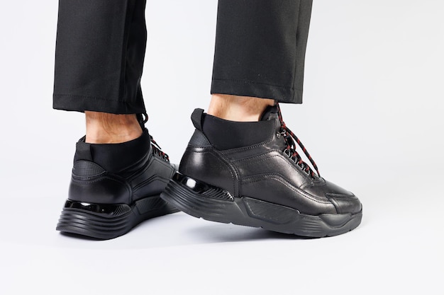 Stilvolle, schwarze, kurze herren-herbst-sneaker aus leder auf weißem hintergrund an den beinen der männer. turnschuhe winterkollektion 2022.