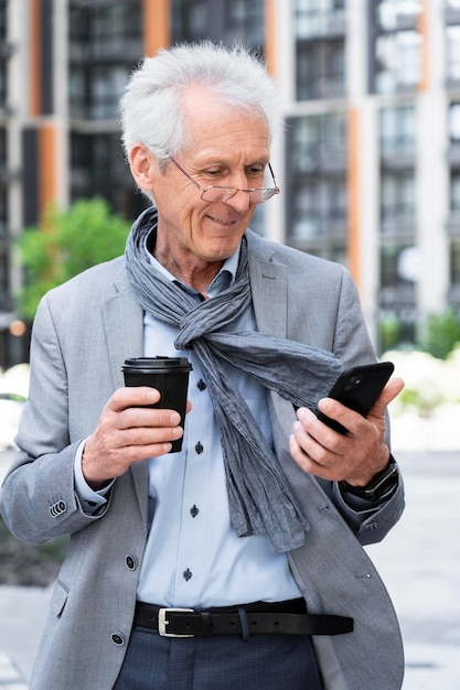 Stilvoller älterer Mann in der Stadt mit Smartphone beim Kaffeetrinken