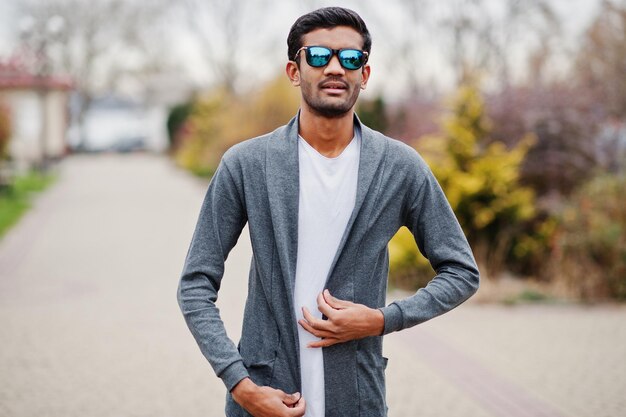 Stilvoller indischer Mann mit Sonnenbrille trägt lässige Posen im Freien