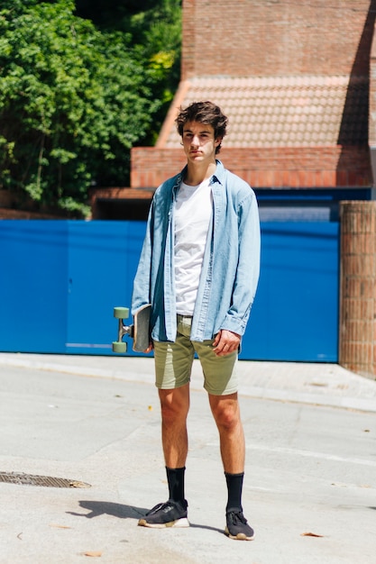 Stilvoller junger Mann, der stehende Außenseite des Skateboards hält