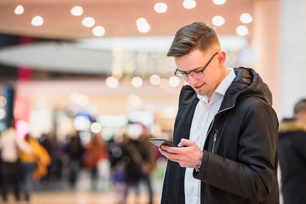 Stilvoller junger Mann im Mall unter Verwendung des Handys