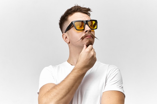 Stilvoller junger Mann mit Sonnenbrille und weißem T-Shirt Denken