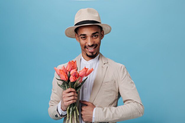 Stilvoller Mann in Anzug und Hut mit Blumenstrauß an blauer Wand