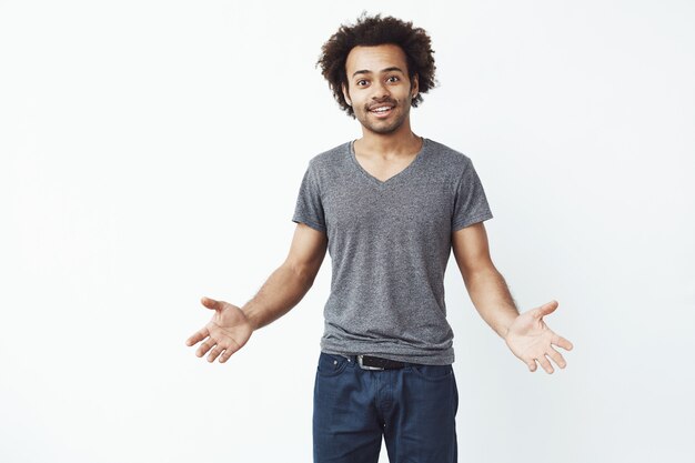 Stilvoller und gutaussehender afrikanischer Mann mit weit geöffneten Armen gegen weiße Wand, die zu einem Auftritt einlädt.