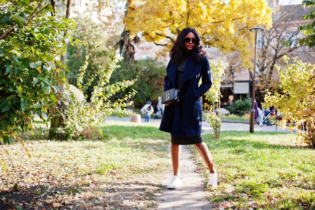 Stilvolles afrikanisch-amerikanisches Mädchen in blauem Mantel und Sonnenbrille posierte am sonnigen Herbsttag Afrika-Modellfrau