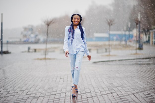 Stilvolles afrikanisch-amerikanisches Mädchen mit Dreadlocks, das bei Schneewetter im Freien ein Handy zur Hand hält