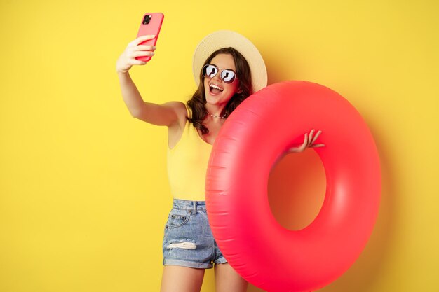 Stilvolles brünettes Mädchen im Urlaub macht Selfie mit Schwimmring und geht am Strand schwimmen im Meer auf Sommer...