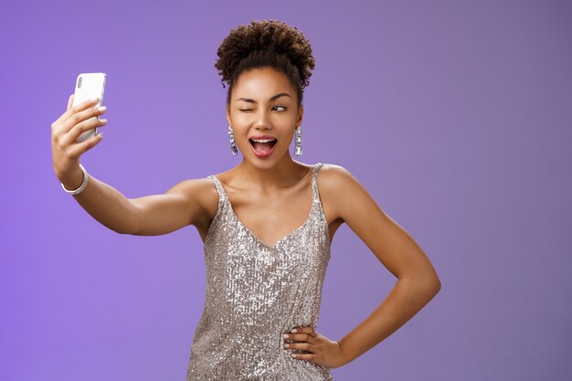 Stilvolles freches afroamerikanisches B-Day-Mädchen, das selfie neues elegantes silbernes glänzendes Kleid nimmt.