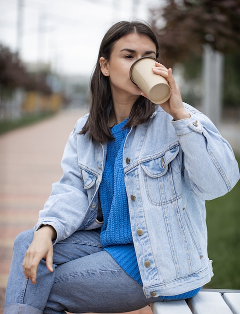 Stilvolles fröhliches Mädchen im lässigen Stil genießt Kaffee zum Mitnehmen bei einem Spaziergang.