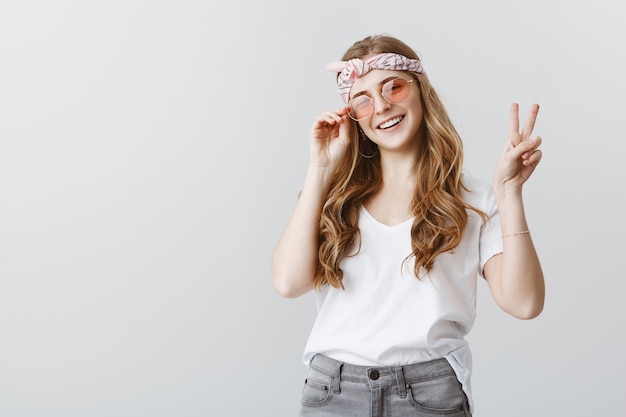 Stilvolles Hipster-Mädchen in der Sonnenbrille, die glücklich lächelt und Friedenszeichen zeigt