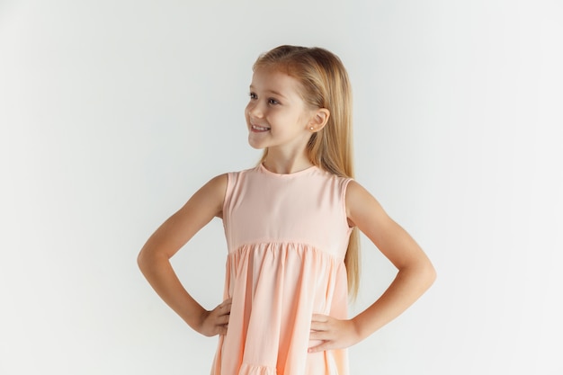 Stilvolles kleines lächelndes Mädchen, das im Kleid lokalisiert auf weißem Studio aufwirft