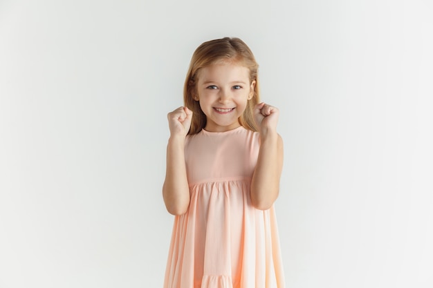 Stilvolles kleines lächelndes Mädchen, das im Kleid lokalisiert auf weißem Studio aufwirft