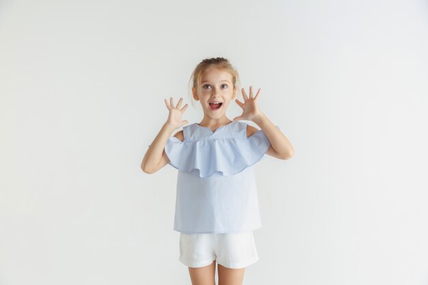 Stilvolles kleines lächelndes Mädchen, das in der Freizeitkleidung lokalisiert auf weißem Raum aufwirft. Kaukasisches blondes weibliches Modell. Menschliche Gefühle, Gesichtsausdruck, Kindheit, Verkauf