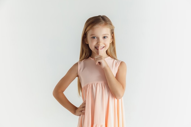 Stilvolles kleines lächelndes Mädchen posiert im Kleid lokalisiert auf weißem Raum. Kaukasisches blondes weibliches Modell. Menschliche Gefühle, Gesichtsausdruck, Kindheit