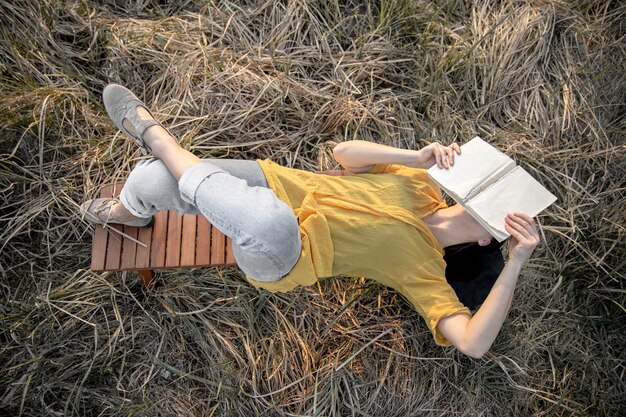 Stilvolles Mädchen mit einem Buch in den Händen liegt im Gras in der Natur.