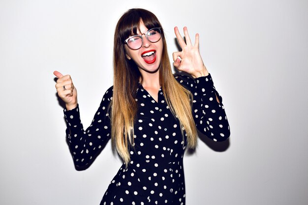 Stilvolles Porträt der jungen Hipster-Frau, die auf weißem Hintergrund, langen Ombre-Haaren, hellem Make-up und klarer Sonnenbrille, Vintage relevantes Kleid aufwirft.