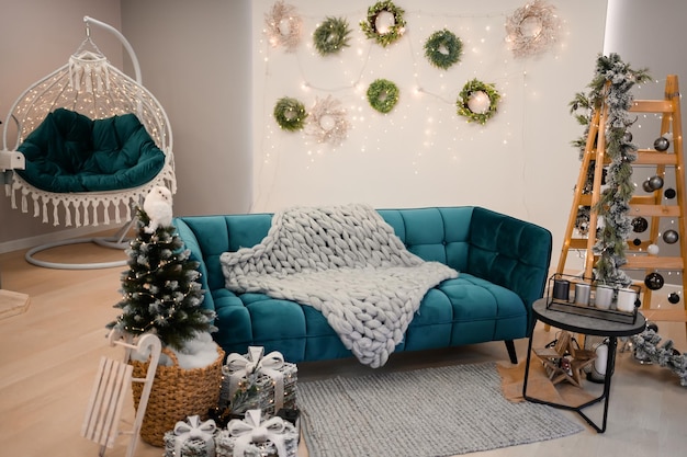 Stilvolles weihnachtswohnzimmer mit grünem sofa, weihnachtsbaum und kranzsternen, geschenken und deko ...
