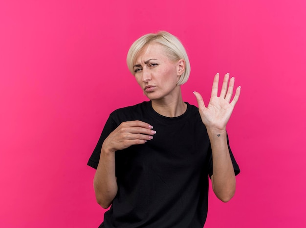 Stirnrunzelnde blonde slawische Frau mittleren Alters, die nach vorne schaut und fünf mit der Hand zeigt, hält eine andere in der Luft isoliert auf rosa Wand mit Kopienraum