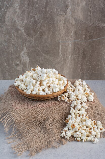 Stoffbezogener Sockel mit einer Schüssel voller Popcorn oben neben einem Popcornhaufen auf Marmor.