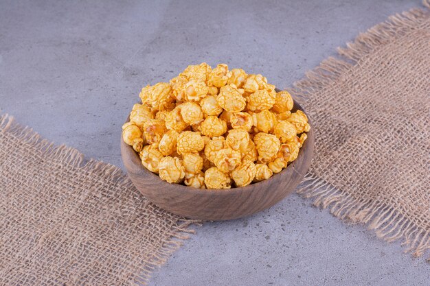 Stoffstücke unter einer Holzschale gefüllt mit aromatisiertem Popcorn auf Marmorhintergrund. Foto in hoher Qualität