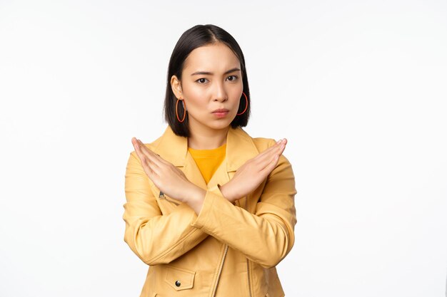 Stop-Geste Ernsthafte asiatische Frau, die Armkreuz macht, verbietet etw, Abneigung abzulehnen und missbilligt die Aktion, die auf weißem Hintergrund steht