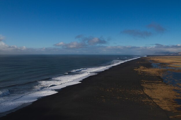Strand umgeben vom Meer mit Hügeln unter einem bewölkten Himmel in Island