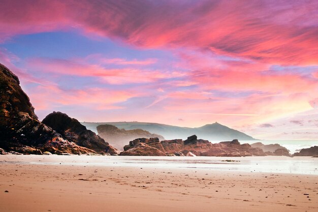 Strand umgeben von Felsen und dem Meer unter einem bewölkten Himmel während eines schönen rosa Sonnenuntergangs