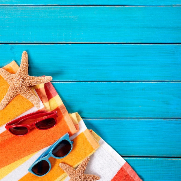 Strandszene mit orange gestreiftem Handtuch, Seestern und Sonnenbrille auf alten blau lackierten Holzterrassen. Platz für Kopie.