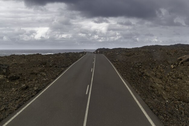 Straße umgeben von Hügeln unter einem bewölkten Himmel im Timanfaya-Nationalpark in Spanien