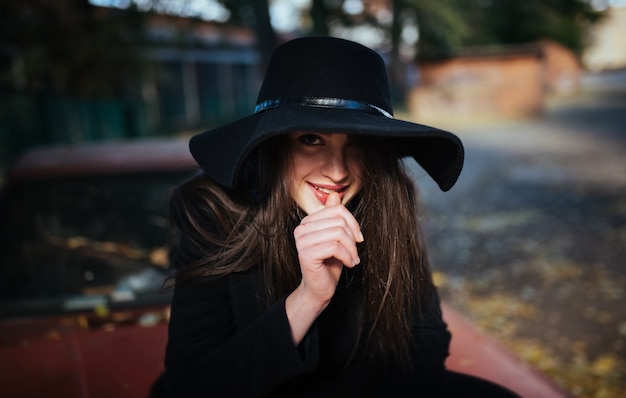 Straßenporträt der jungen zufälligen Dame im Hut mit, schwarze Kleidung, rote Lippen