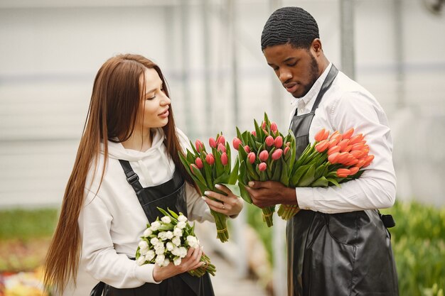 Strauß Tulpen in einem Kerl. Mann und Frau in einem Gewächshaus. Gärtner in Schürzen.