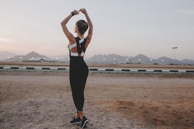 Strecken auf Straße im tropischen Land der freudigen schönen Frau auf Sonnenuntergang. Sonnenschein genießen, im Freien trainieren, Sommer, starke Sportlerin, Energie, Motivation, gesunder Lebensstil.