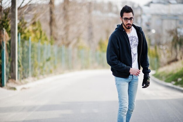 Street Style arabischer Mann mit Brille mit Longboard Longboarding die Straße hinunter