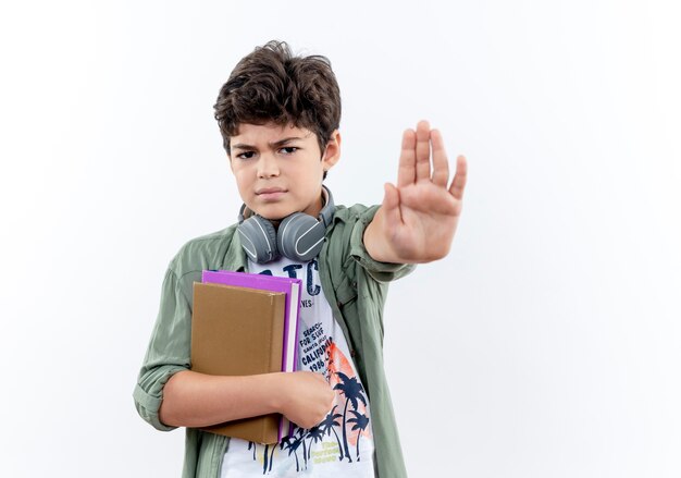 Strenger kleiner Schuljunge, der Buch hält und Stoppgeste zeigt, die auf Weiß isoliert wird