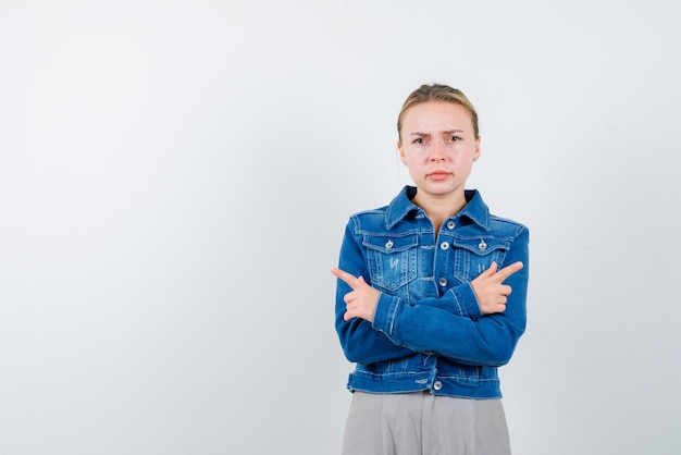 Strenges junges Mädchen, das ihre Arme verschränkt und beide Seiten auf weißem Hintergrund zeigt