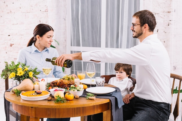 Strömender wein des mannes im glas beim speisen mit familie