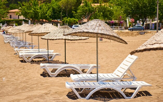 Stroh-Sonnenschirme mit Liegestühlen am Strand