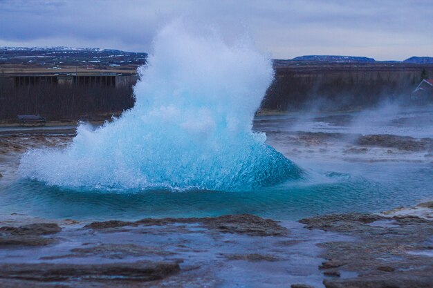 Strokkur Geysir, umgeben von Hügeln unter bewölktem Himmel am Abend in Island