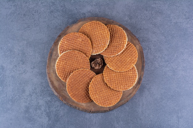 Stroopwafels mit Tannenzapfen isoliert in einer Holzplatte auf Stein. Hochwertiges Foto