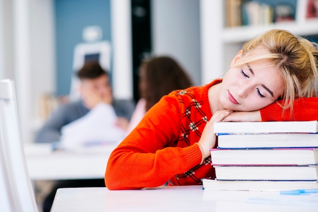 Student, der auf Büchern auf Tabelle in der Bibliothek Nickerchen macht