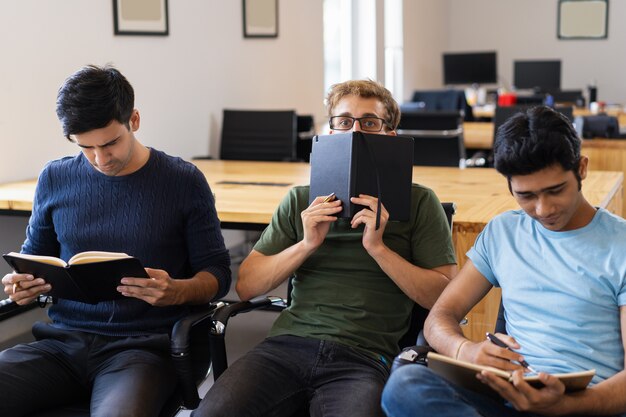 Student, der hinter Notizbuch sich versteckt und zwischen zwei Freunden sitzt