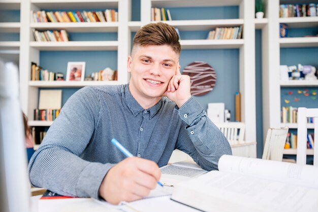 Student, der mit Büchern und Stift in der Bibliothek sitzt