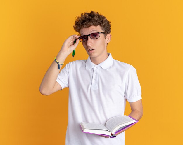 Student in Freizeitkleidung mit Brille mit Buch und Bleistift, die überrascht in die Kamera schaut