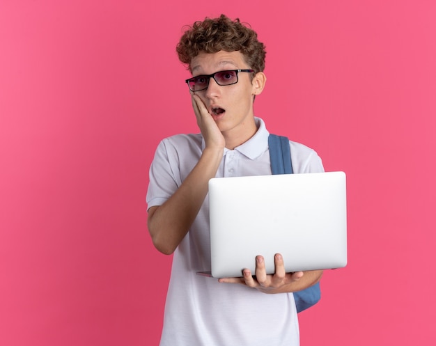 Student in Freizeitkleidung mit Brille mit Rucksack mit Laptop und Blick in die Kamera erstaunt überrascht