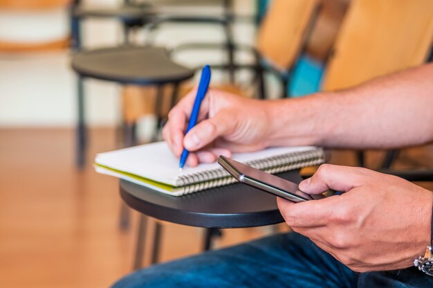 Student mit einem Smartphone während des Studiums / Student mit Martphone Sucht Konzept. Technologie-Konzept - Student Blick auf Telefon und etwas schreiben